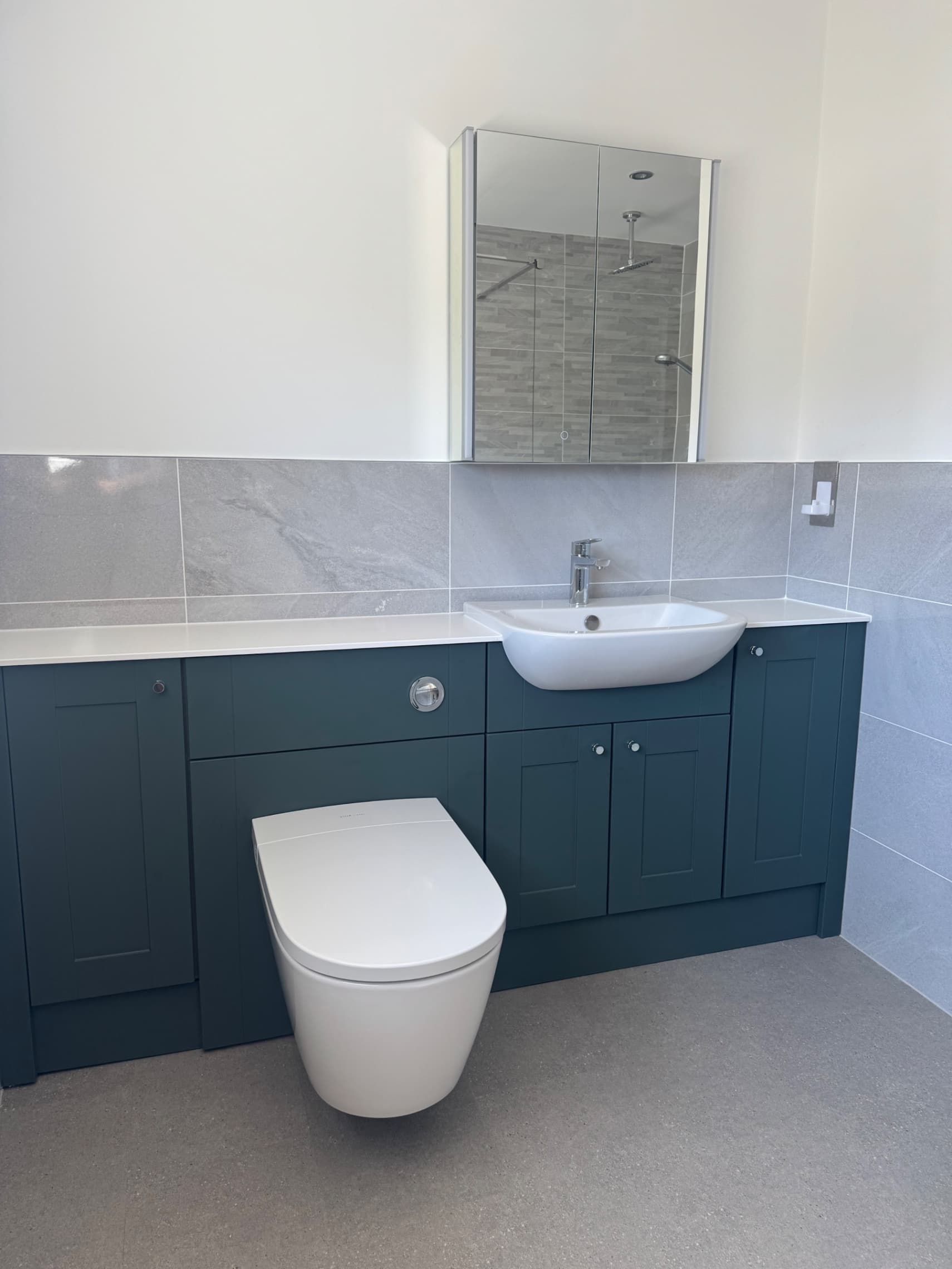 We've completed this bathroom refurbishment with a stylish dark green vanity unit, white basin and toilet, grey wall tiling, and a frameless shower screen—everything is now finished and ready for our customer to enjoy.