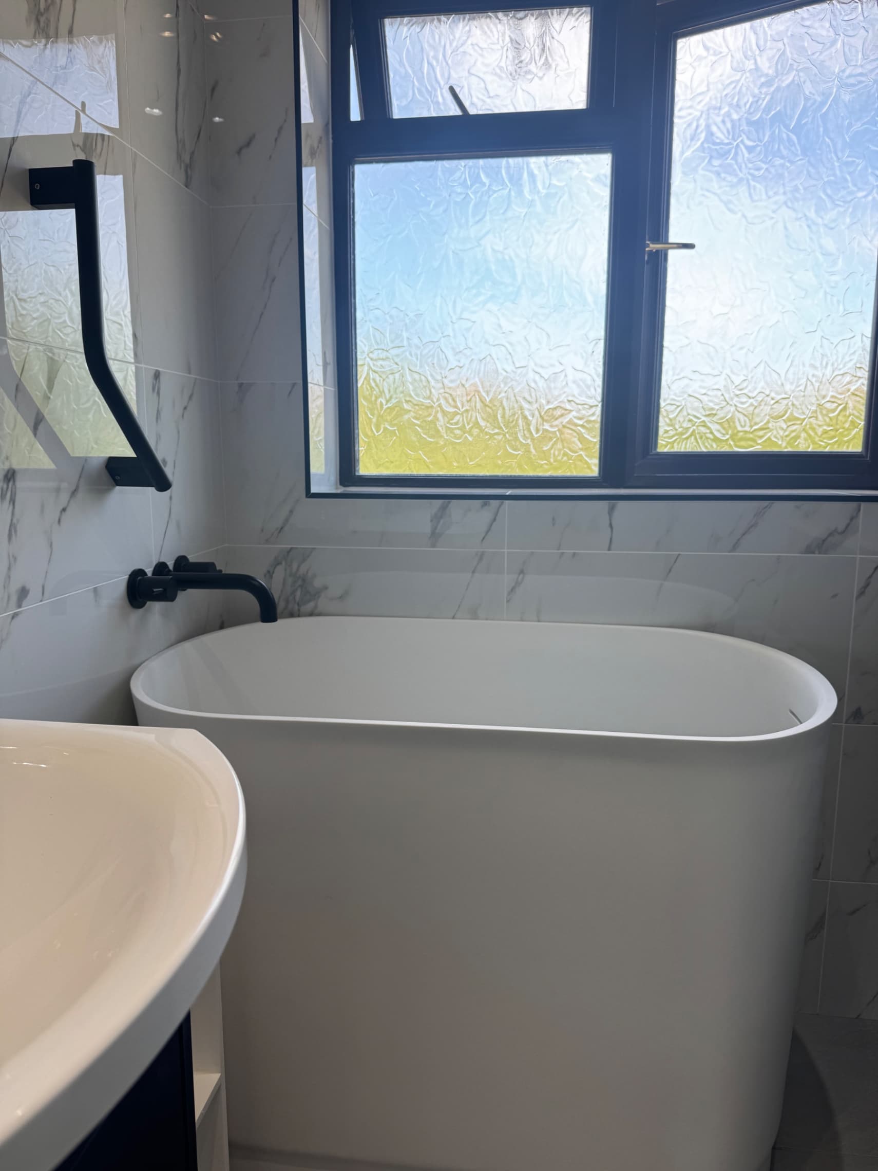 We've completed this beautiful bathroom with a freestanding bath as the centrepiece and fitted a grab rail for accessibility and safety. The marble-effect tiling and black fixtures create a clean, modern finish that our customers love.