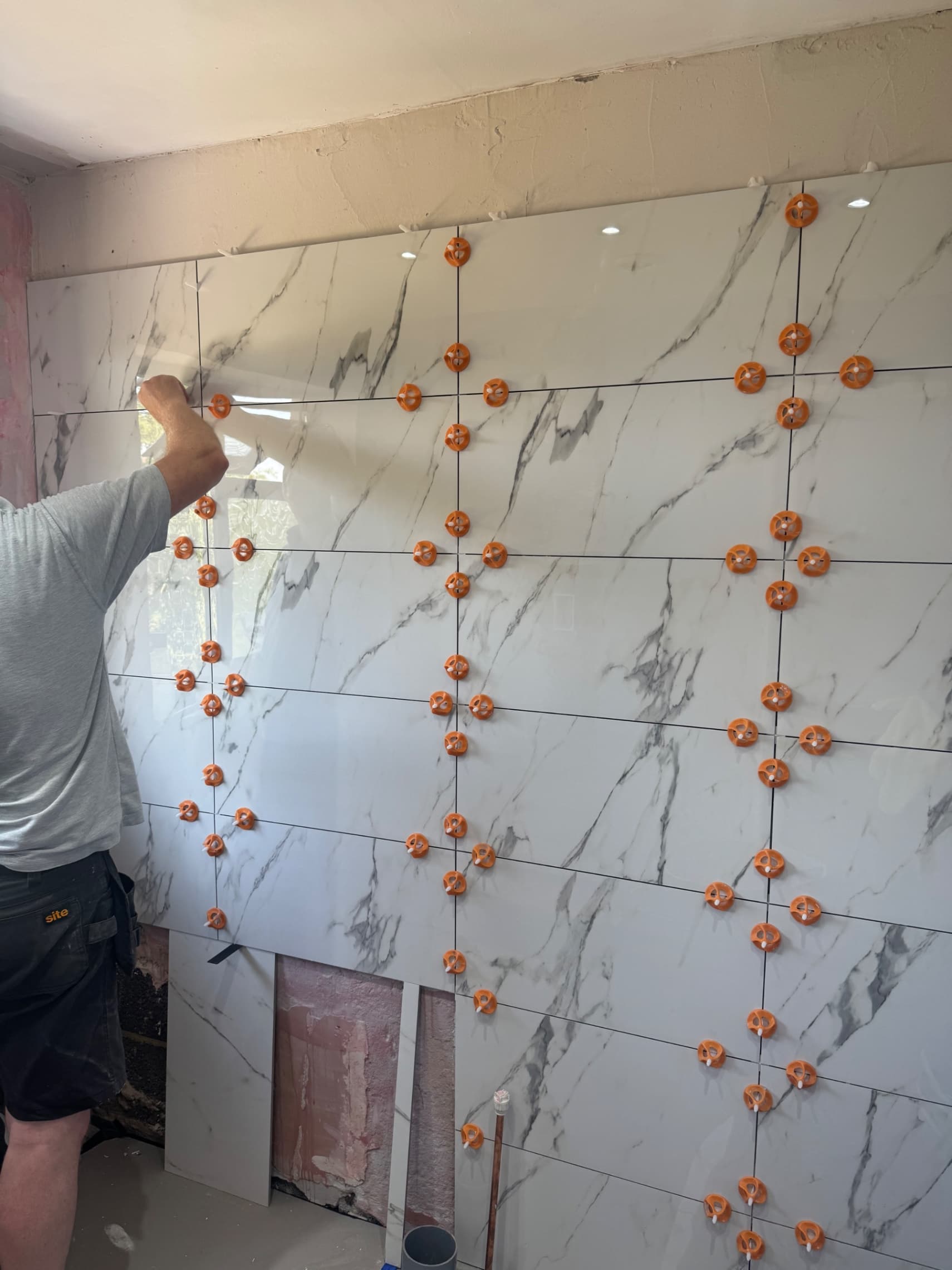 We're well into the tiling on this bathroom, laying 60x30cm marble effect porcelain tiles across the wall. The levelling clips keeping everything perfectly flat as we work through the installation.